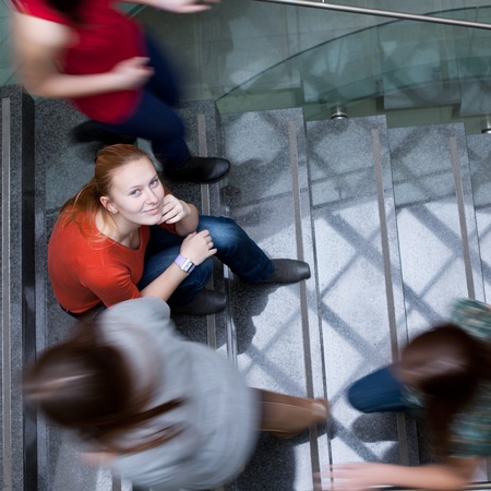 At the university/college - Students rushing up and down a busy stairway - confident pretty young female student looking upwards (color toned image)の写真素材