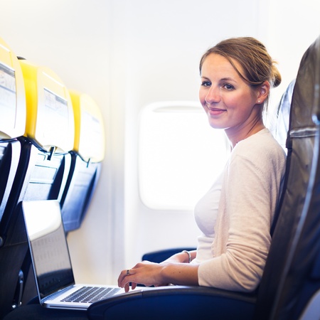 Young woman working on her laptop computer on board of an airplane during the flight