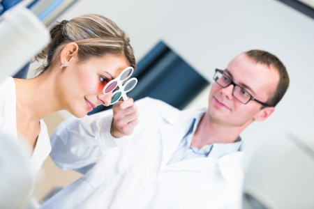 Optometry concept - pretty young woman having her eyes examined by an eye doctor/optometrist (color toned image; shallow DOF)の写真素材