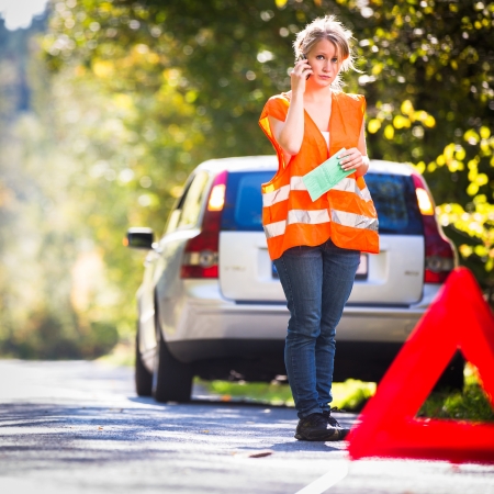 Young female driver wearing a high visibility vest, calling the roadside service/assistance after her car has broken downの写真素材