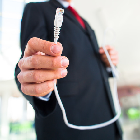 Young businessman holding an ethernet cable - stressing the importance of fast and reliable internet connection for a business (color toned image; shallow DOF)の写真素材