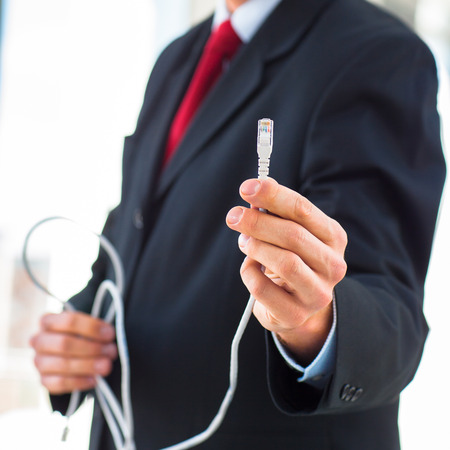 Young businessman holding an ethernet cable - stressing the importance of fast and reliable internet connection for a business (color toned image; shallow DOF)の写真素材