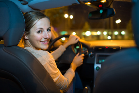 Pretty young woman driving her new car at nightの写真素材
