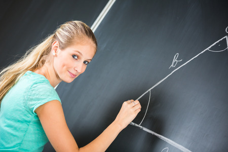 Pretty young elementary school/college teacher writing on the chalkboard/blackboa rd during a math class (color toned image; shallow DOF)の写真素材