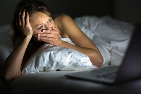 Pretty young woman watching something awful sad on her laptop in bed