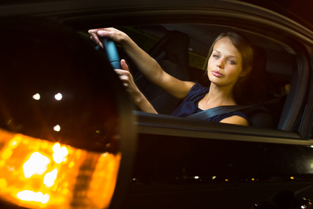 Driving a car at night - pretty, young woman driving her modern car at night, in a city の写真素材