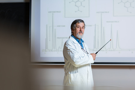 Senior chemistry professor giving a lecture in front of classroom full of students 