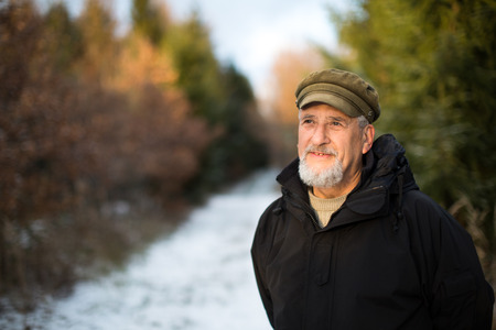 Portrait of a senior man, outdoor on a snowy forest path. Enjoying the crisp fresh air, watching the Sun go down.の写真素材