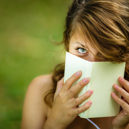 Cute young woman  covering her face with a book she is readingの写真素材