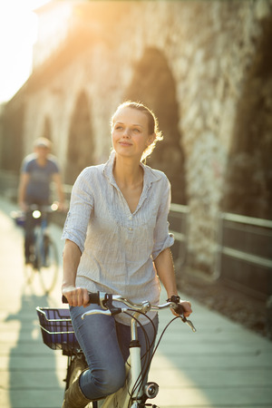 Pretty, young woman riding a bicycle in a city with her boyfriend (color toned image; shallow DOF)の写真素材
