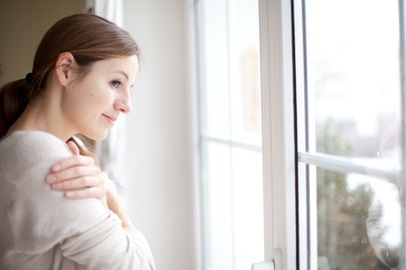 Woman lookong from a window of her house on a cold and snowy winter dayの写真素材