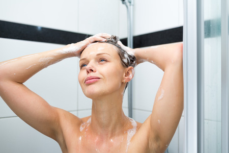 Young woman washing her hair with shampoo, taking a hot long shower
