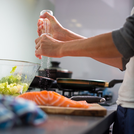 Young woman seasoning a salomn filet in her modern kitchen, preaparing a healthy foodの写真素材