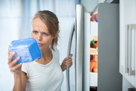 Is this still fine? Pretty, young woman in her kitchen by the fridge, looking at the expiry date of a product she took from her fridge -の写真素材