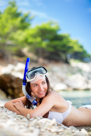 Pretty, young woman on a beach during her summer vacation with snorkel lying on beach with snorkeling mask and fins smiling happy enjoying the sun on a sunny summer day.の写真素材