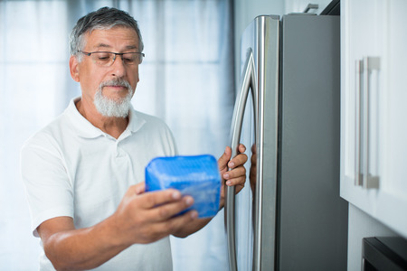 Is this still fine? Senior man in his kitchen by the fridge, looking at the expiry date of a product she took from her fridge -の写真素材