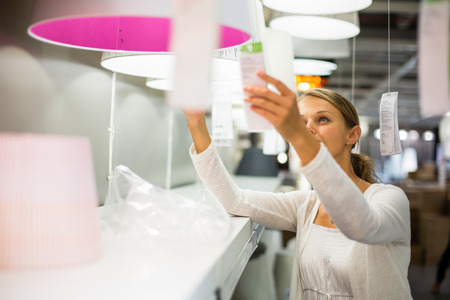 Pretty, young woman choosing the right light for her apartment in a modern home furnishings store (color toned image; shallow DOF)の写真素材