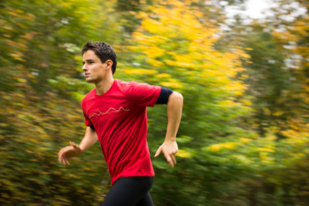 Young man running outdoors in a city park on a fall/autumn day (motion blurred image)の写真素材