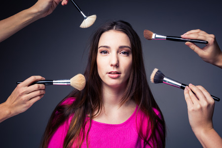 Pretty, young woman in the able care of professional make-up artists (color toned image) - hands with brushes around her, she is going to look awesomeの写真素材