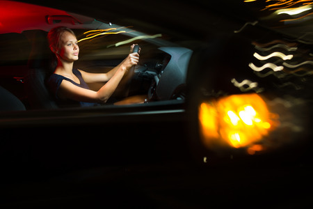 Driving a car at night - pretty, young woman driving her modern car at night, in a city (shallow...