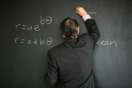 Senior male teacher teaching mathematics, writing on the blackboardの写真素材