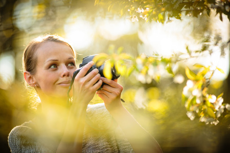 Pretty female amateur photographer taking photos outdoors, doing what she loves to do