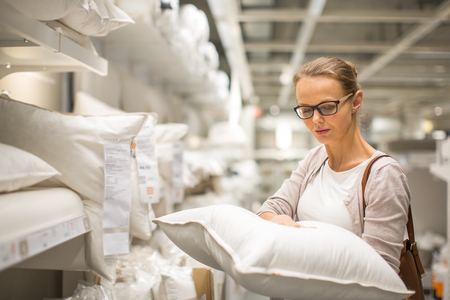 Pretty, young woman choosing the right pillow for her bed in a modern home furnishings store (color toned image; shallow DOF)の写真素材
