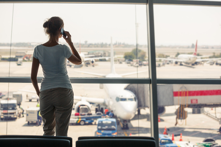 Pretty, young woman waiting at a gate area of a modern airport for  the boarding call - making some calls(color toned image; shallow DOF)の写真素材