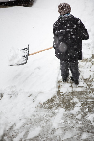 Man shoveling snow from the sidewalk in front of his house after a heavy snowfall in a cityの写真素材