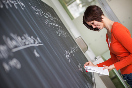 Pretty young college student/young teacher writing on the chalkboard/blackboard during a math class...
