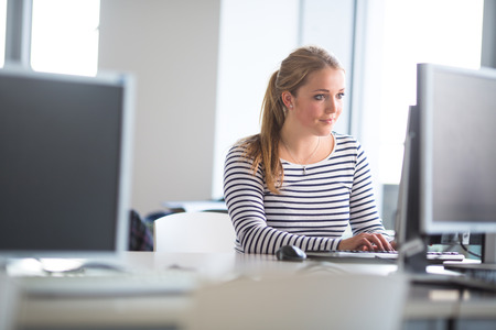 Pretty, female student looking at a desktop computer screen, learning unpleasant news about her exam results. University/office/school conceptの写真素材