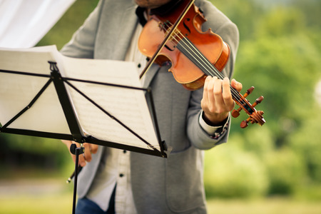 Male violinist playing his instrument and reading a music sheet during an outdoor summer wedding ceremony (shallow DOF; color toned image)の写真素材