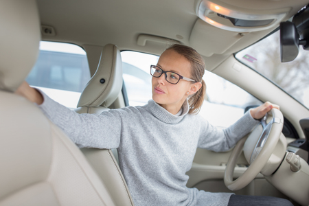 Woman driving a car - female driver at a wheel of a modern car, parking, going in reverse using the parking sensors (DOF; color toned image)の写真素材
