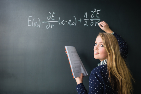 Pretty, young college student writing on the chalkboard/blackboard during a math class (colort toned...