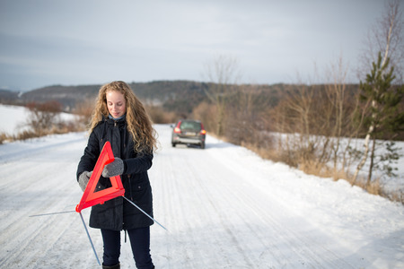 Young woman setting up a warning triangle and calling for assistance after her car broke down in the middle of nowhere on a freezing winter dayの写真素材