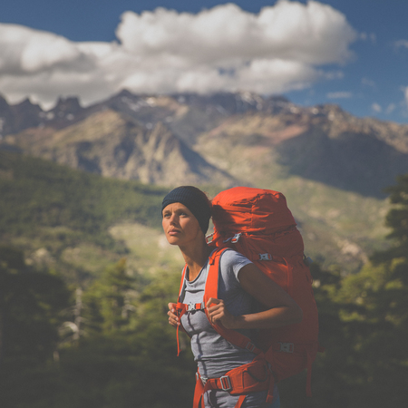 Pretty, female hiker in high mountains packing her backpack