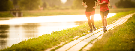 Couple running outdoors, at sunset, by a river, staying active and fitの写真素材