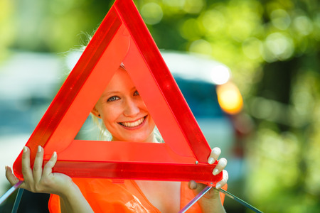 Young female driver wearing a high visibility vest, calling the roadside service/assistance after...