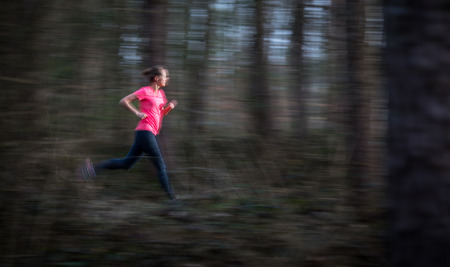Young woman running outdoors in a forest, going fast (motion blurred image)の写真素材