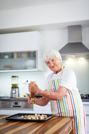 Senior woman cooking in the kitchen - eating and cooking healthy for her family; putting some potates in the oven, enjoying active retirement (shallow DOF; color toned image)の写真素材
