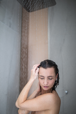 Woman taking a long hot shower washing her hair in a modern design bathroomの写真素材