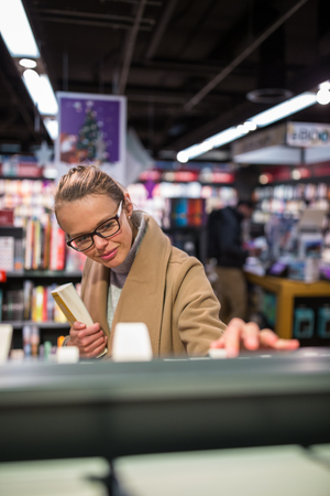 Pretty, young female choosing a good book to buy in a bookstoreの写真素材