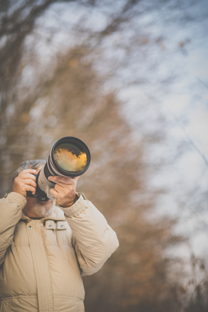 Senior man devoting time to his favorite hobby - photography - taking photos outdoor with his digital camera/DSLR and a big telephoto lensの写真素材