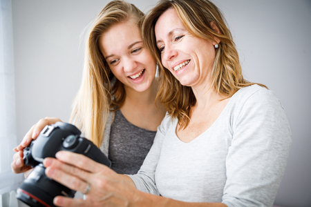 Mother and daughter taking photos and checking them on a modern digital DSLR cameraの写真素材