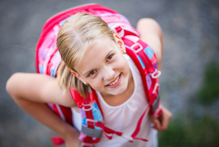Cute little girl going home from school with her backpack full of books looking up with a lovely smileの写真素材