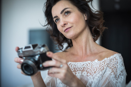 Pretty, young female photographer in her studio taking photos with a vintage film camera (color toned image)の写真素材