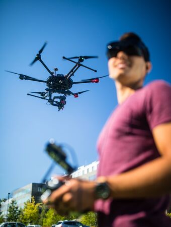 Handsome young man flying a drone outdoors using a VR/augmented reality glasses to operate the...