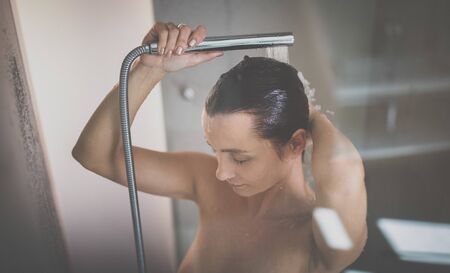 Woman taking a long hot shower washing her hair in a modern design bathroom