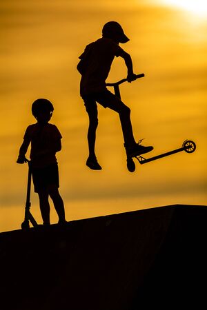 Silhouette of little boys riding scooters against the background of a sea sunset