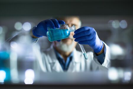 Senior male researcher carrying out scientific research in a lab (shallow DOF; color toned image)の写真素材